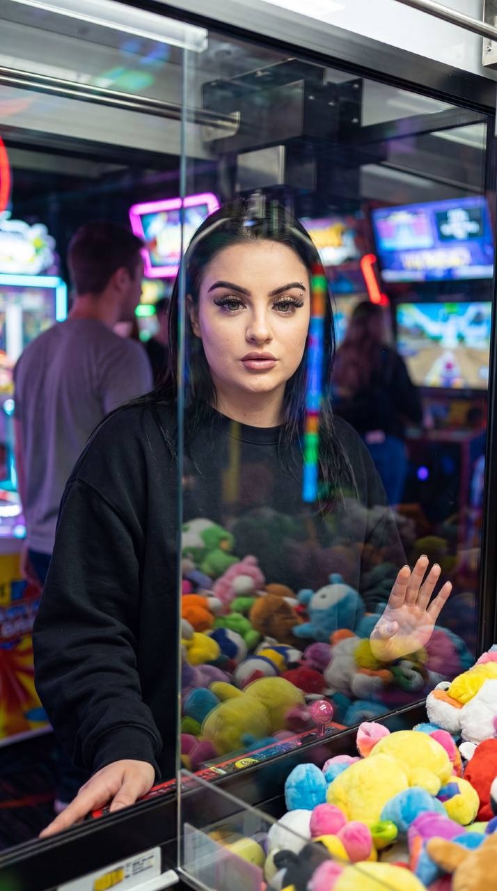 Девушка у автомата с плюшевыми игрушками в аркаде